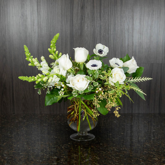 a garden style flower arrangement with all white flowers in a glass footed vase