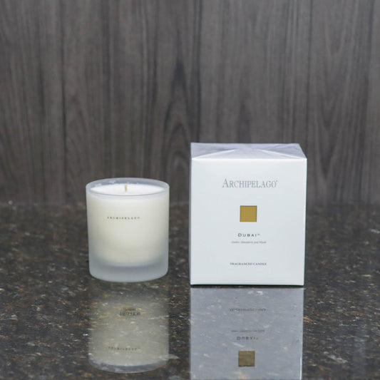 a candle in a frosted glass votive next to the white box it comes packaged in