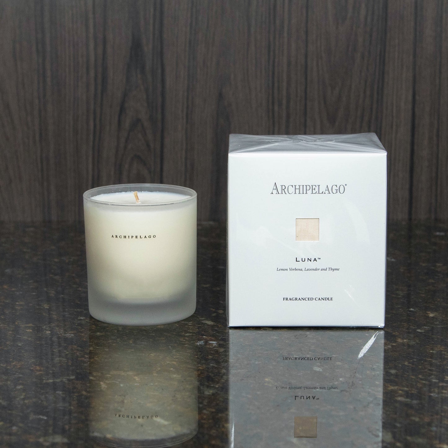 a candle in a frosted glass votive next to the white box it comes packaged in