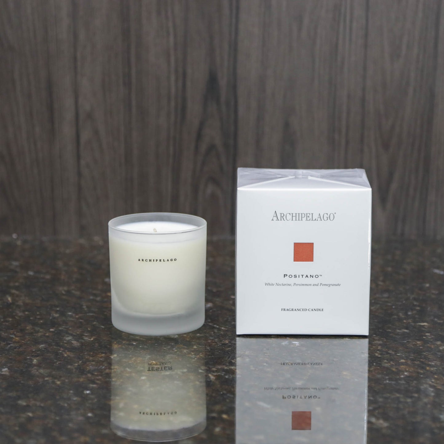 a candle in a frosted glass votive next to the white box it comes packaged in