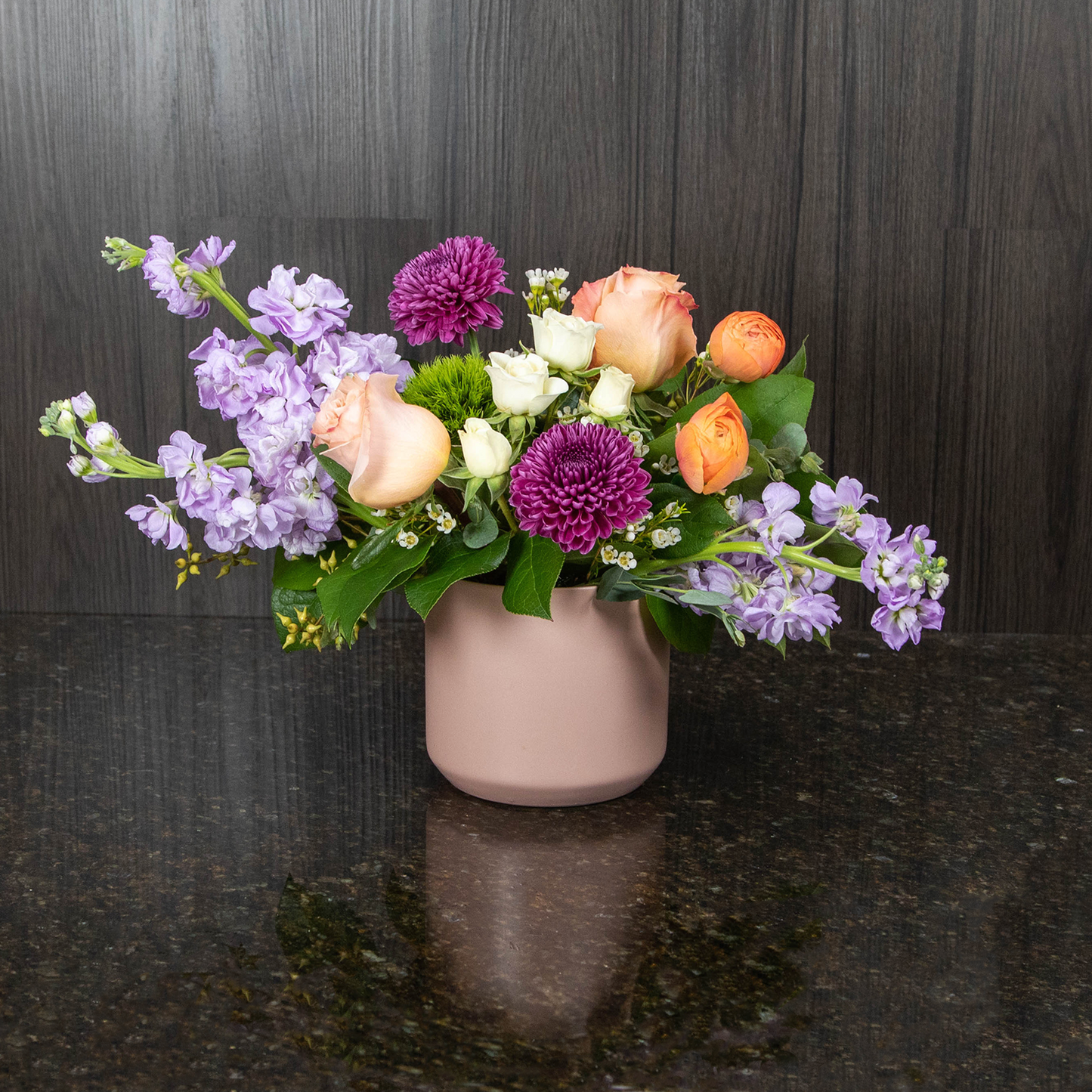 a gardeny flower arrangement with soft colored flowers in a light pink ceramic pot