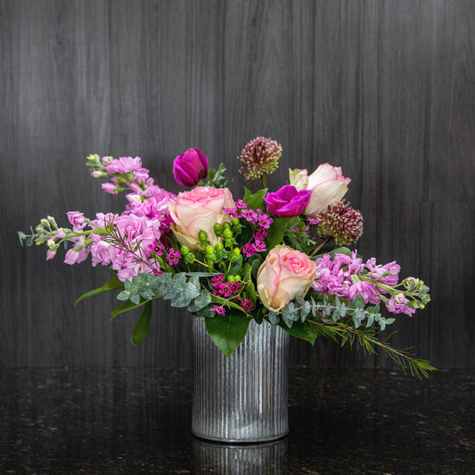 a flower arrangement featuring a variety of pink colored flowers in a corrugated metal container