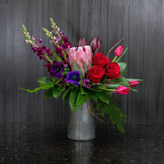 a flower arrangement with dark colored flowers in a corrugated metal container