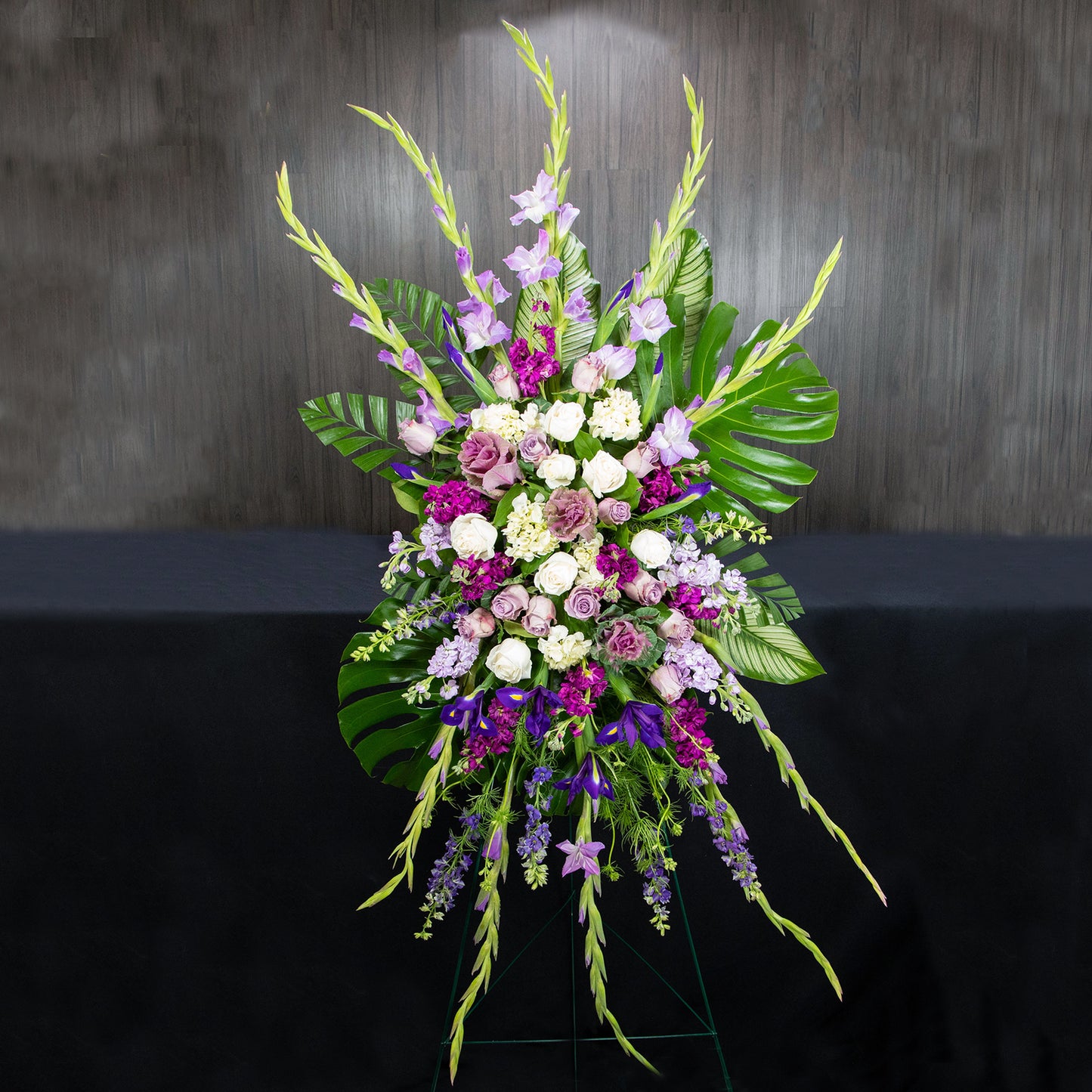 a large funeral easel spray with a variety of purple and white flowers and types of leaves