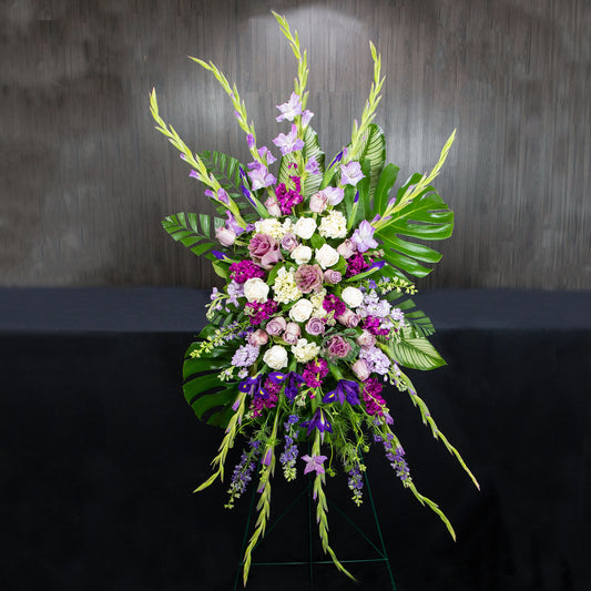 a large funeral easel spray with a variety of purple and white flowers and types of leaves