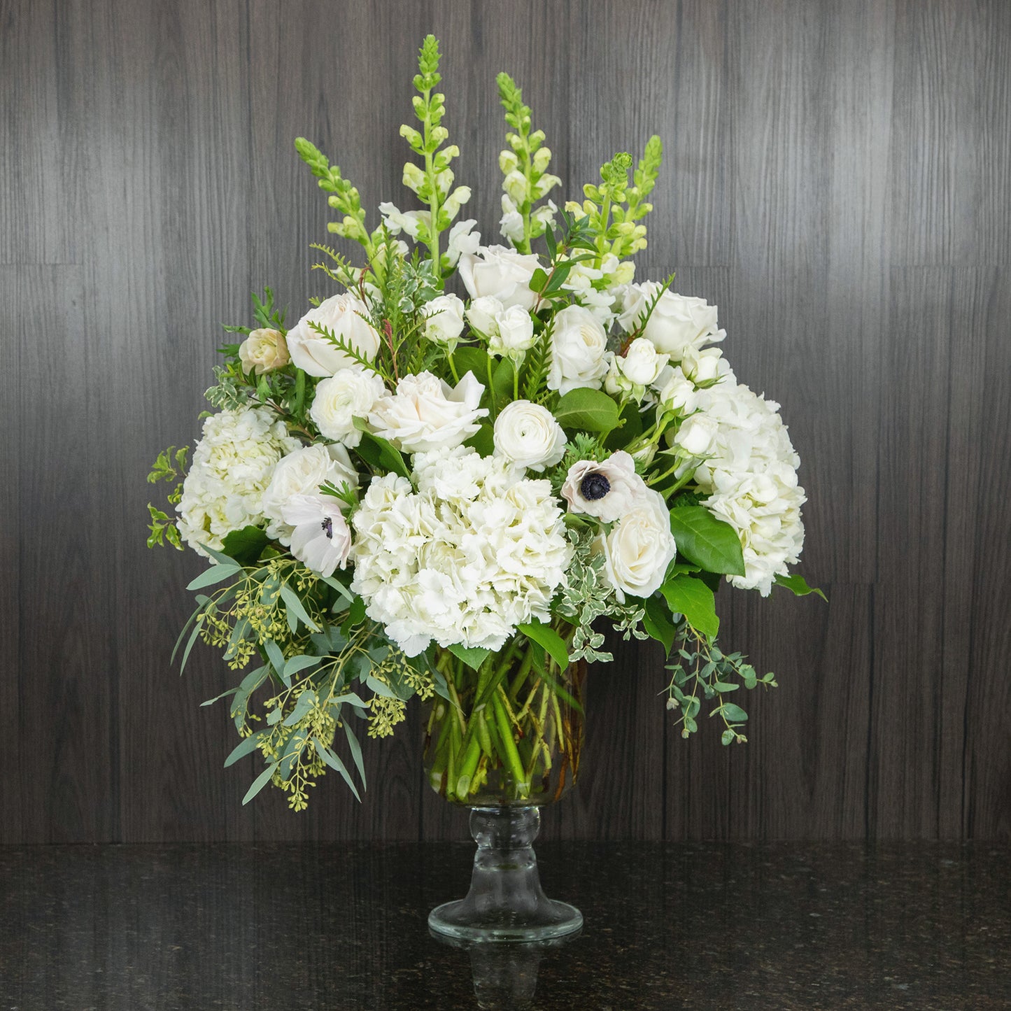 a large flower arrangement with all white flowers in a footed glass vase