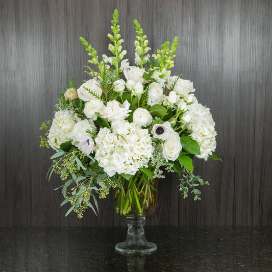 a large flower arrangement with all white flowers in a footed glass vase