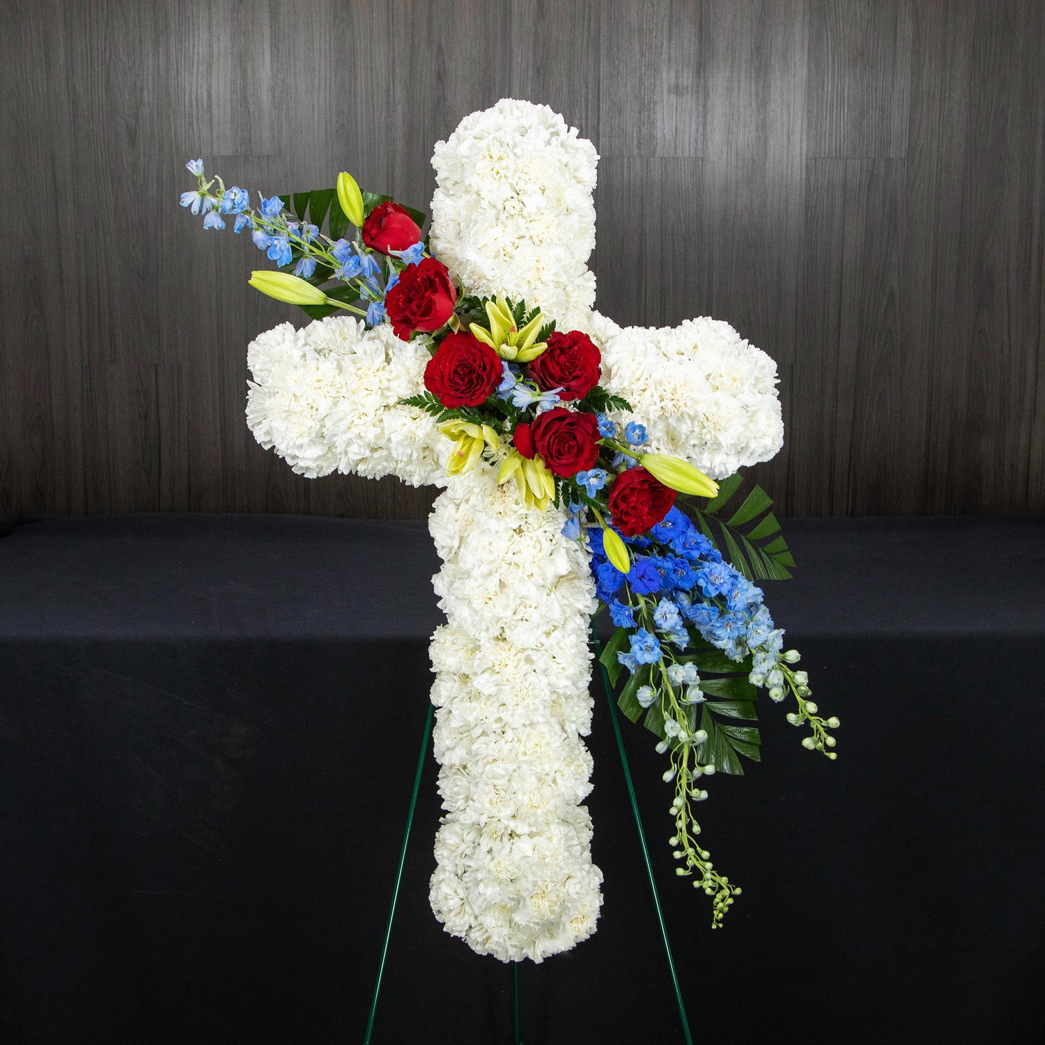 a white floral cross with a belt of red and blue flowers going diagonally across the middle