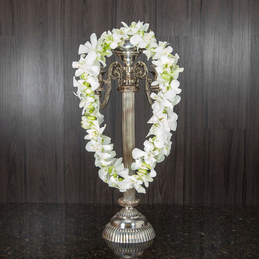a single orchid lei made out of white dendrobium orchids hanging across a candelabra