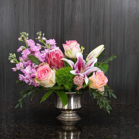 a pink, white, and green flower arrangement in a footed metal container