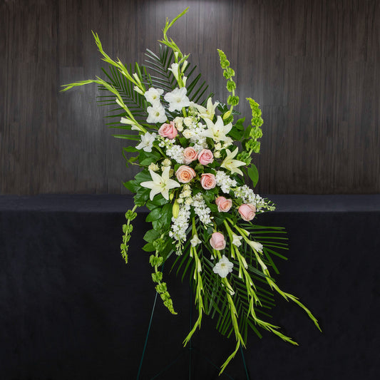 a long and tall funeral easel made with green, white, and pink flowers