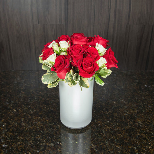 a dozen red roses with white teacup roses in a tall white ceramic vase viewed from the top