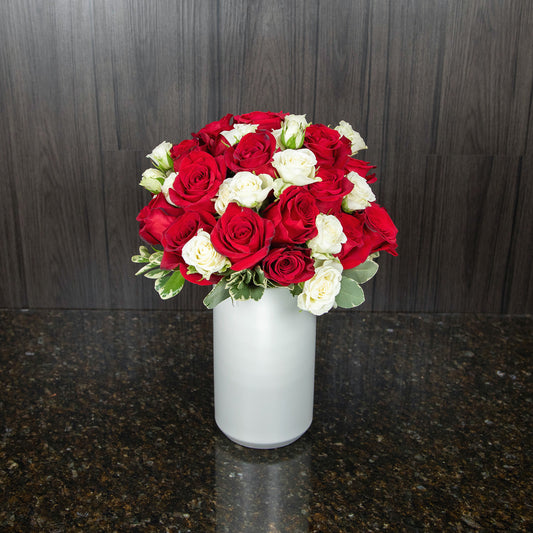 two dozen red roses with white teacup roses in a tall white ceramic vase viewed from the top