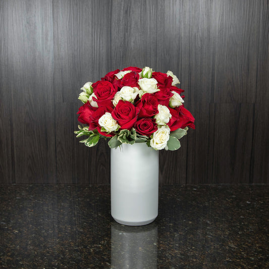 two dozen red roses with white teacup roses in a tall white ceramic vase