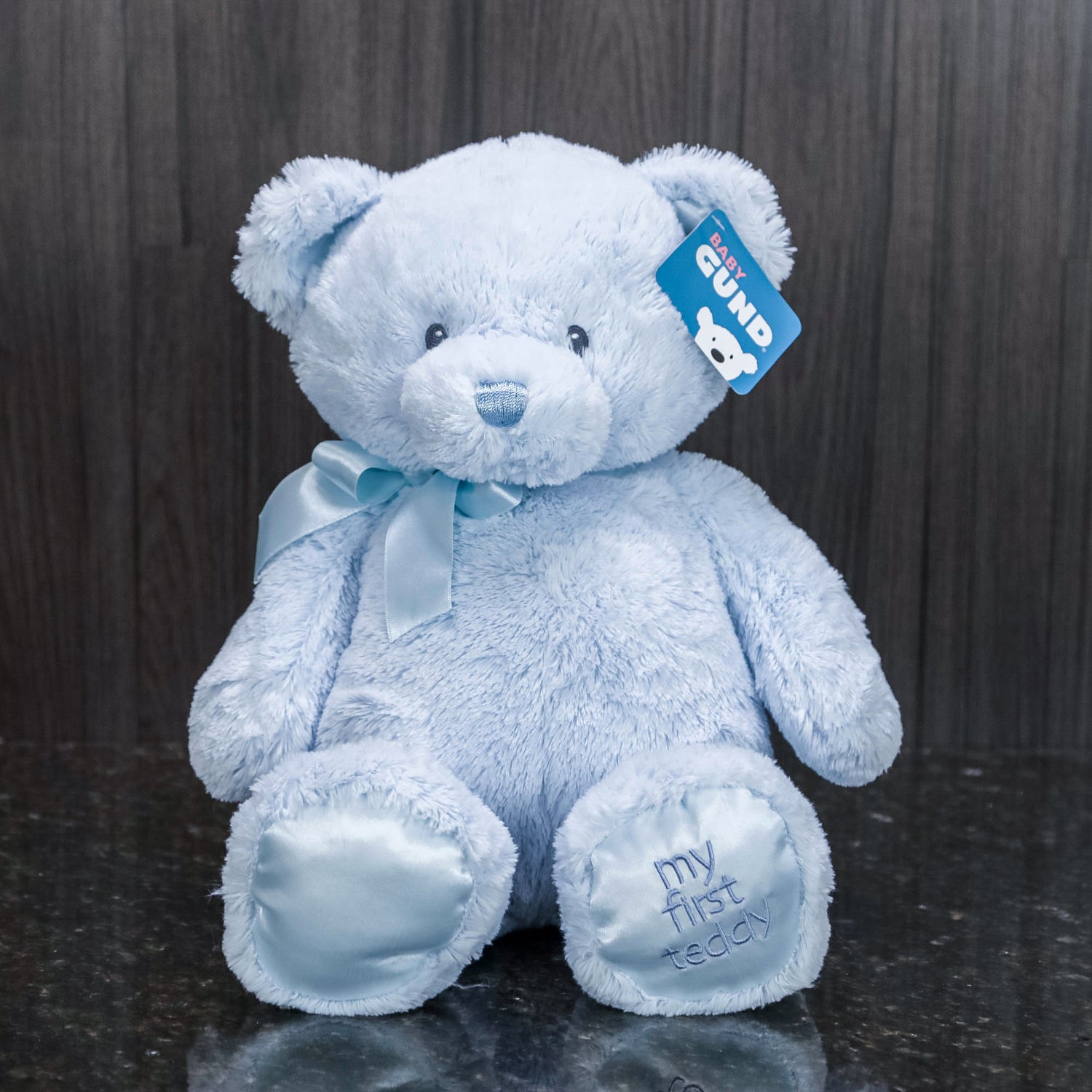 a blue teddy bear with "my first teddy" embroidered on its foot