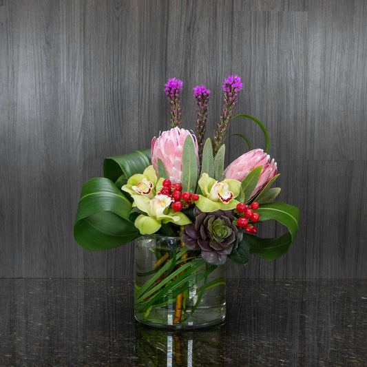 a low tropical arrangement in a glass cylinder vase