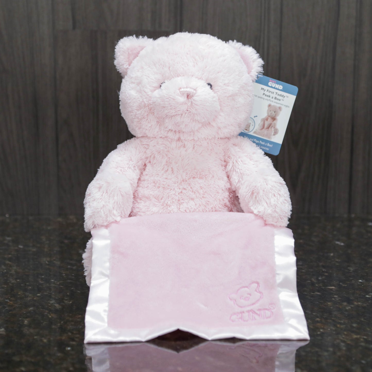 a pink teddy bear holding a blue satin blanket