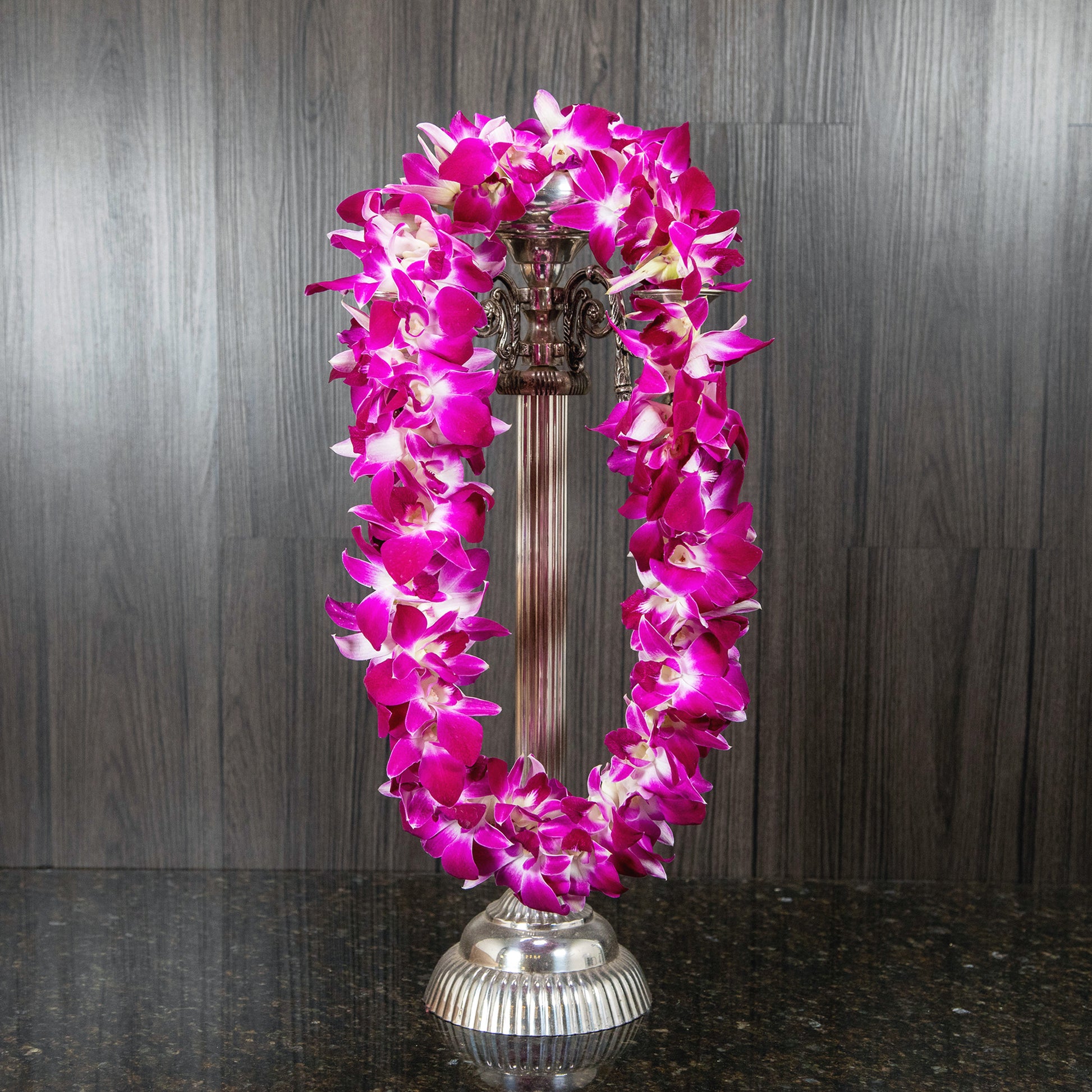 a double purple orchid lei hanging on a silver candelabra