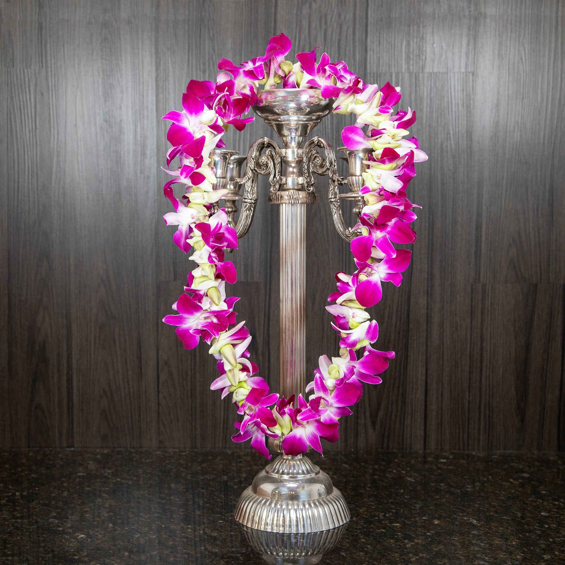 a purple orchid lei strung around a silver candelabra