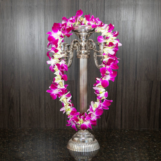 a purple orchid lei strung around a silver candelabra