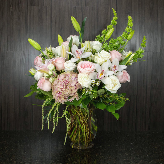 a large flower arrangement with white, pink, and green flowers in a glass vase