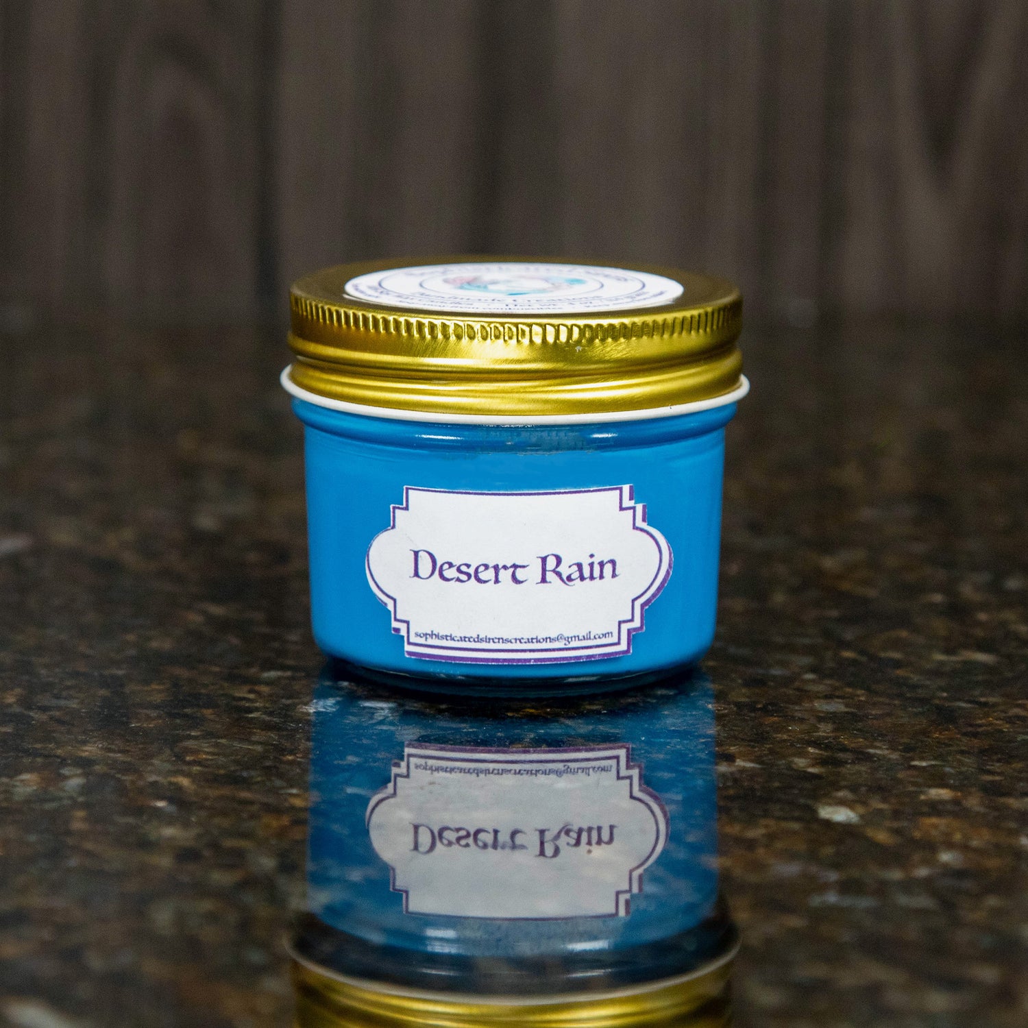a blue candle with a gold lid and a label that reads "desert rain"