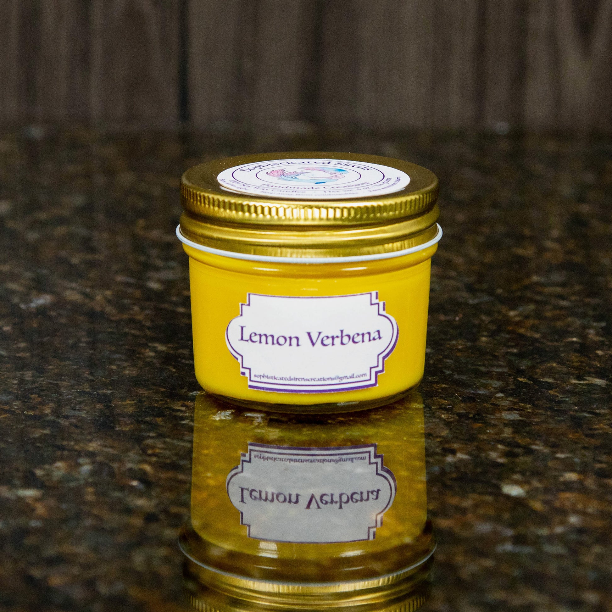 a yellow candle with a gold lid and a label that reads "lemongrass verbena"