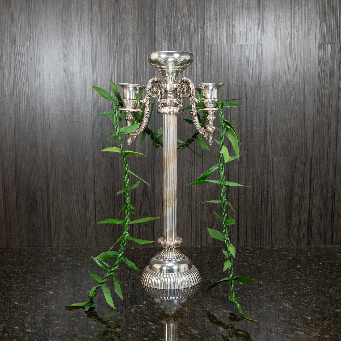 a single maile ti leaf lei hung over a silver candelabra