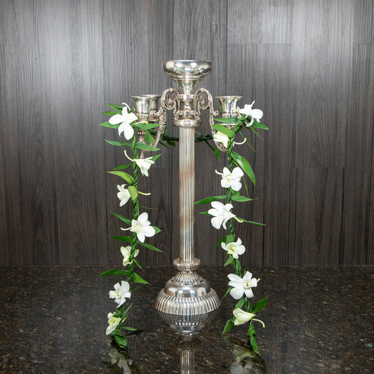 a single maile ti leaf lei with white dendrobium orchid blooms hung over a silver candelabra