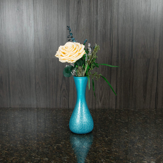 a single large preserved cream rose and preserved greenery in a blue sparkling vase