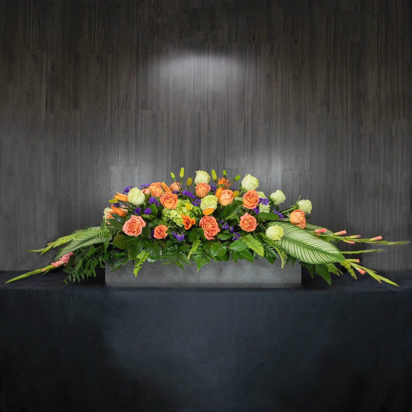 a full casket spray made with orange, green, white, and purple flowers