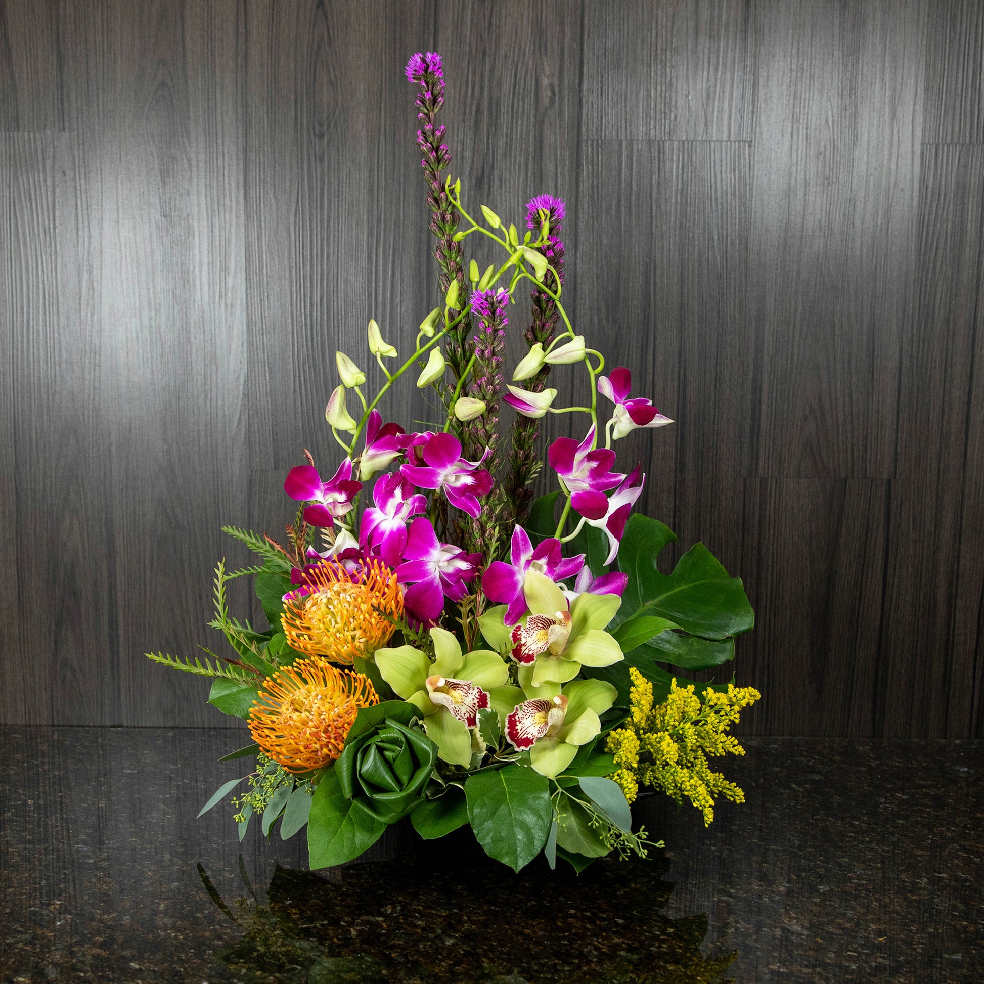 a tropical flower arrangement with a mix of colors in a low black resin tray