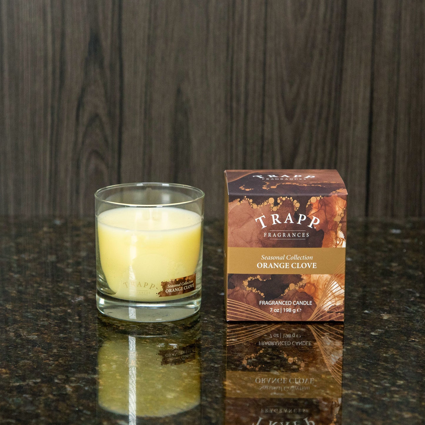 a orange clove scented candle next to the brown box it comes in