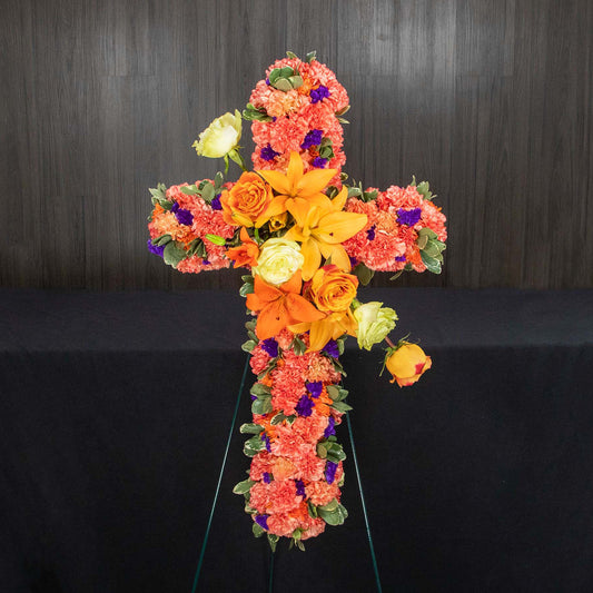 a cross shaped flower easel made with orange flowers and pops of purple and white