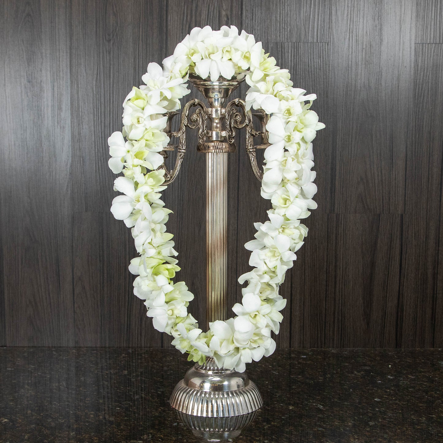 a double orchid lei made out of white dendrobium orchids hanging across a candelabra