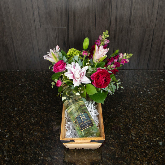 a wooden basket that contains a flower arrangement and a bottle of white wine